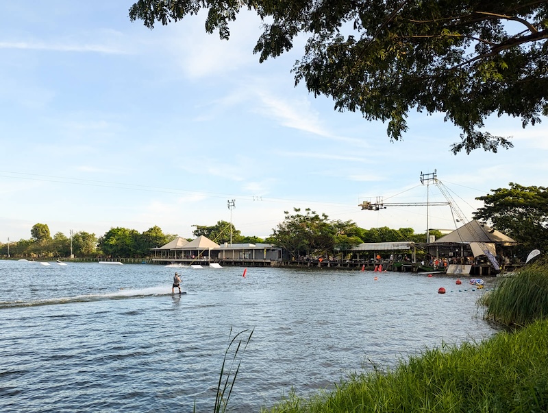 View of the lake at Taco Lake in Bangkok, featuring wakeboarding ramps and the cable section and trees showing a lush area.