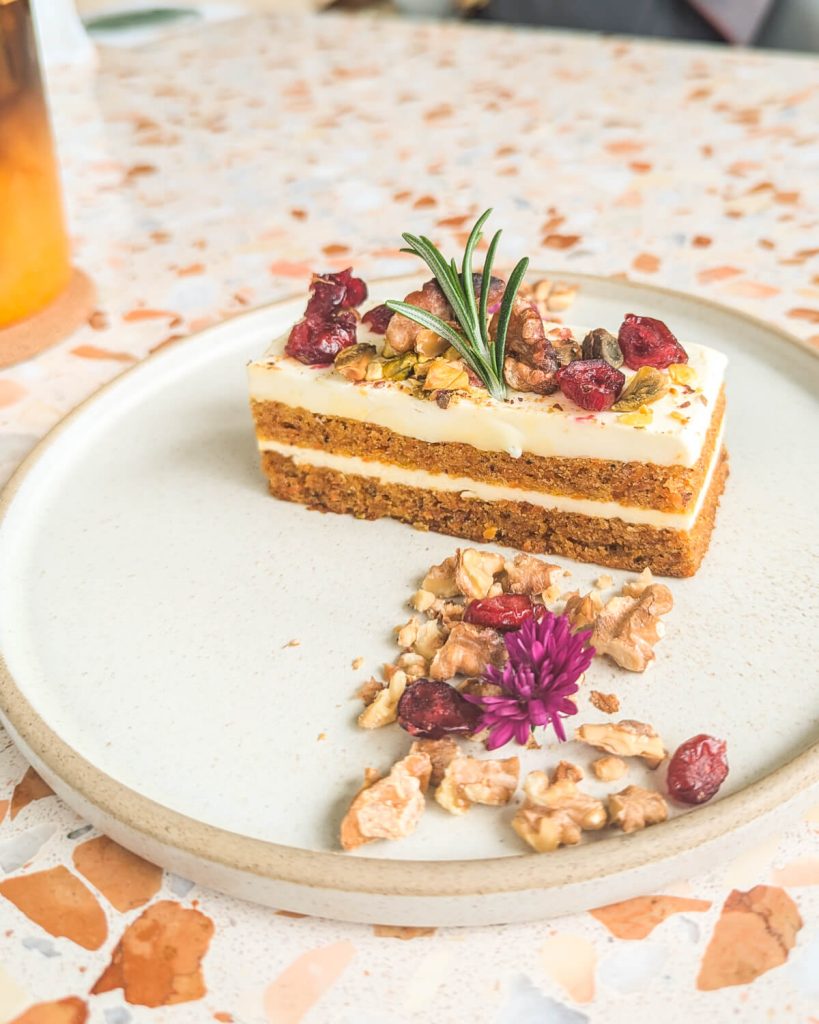 The delicious coffee cake, with two layers of cream cheese frosting, with nuts and edible flowers and dried cranberries