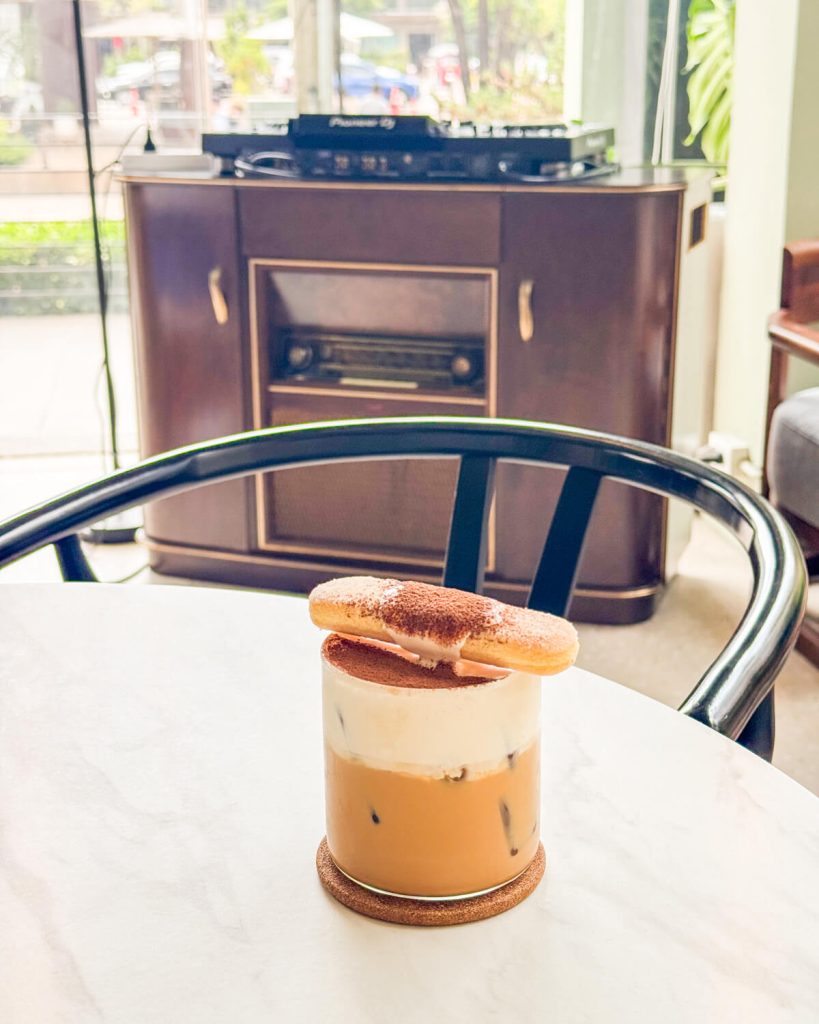 Tiramisu coffee at KIF with a cookie on top and turntables visible in the background, showing the day-to-night transformation of this cafe-meets-bar
