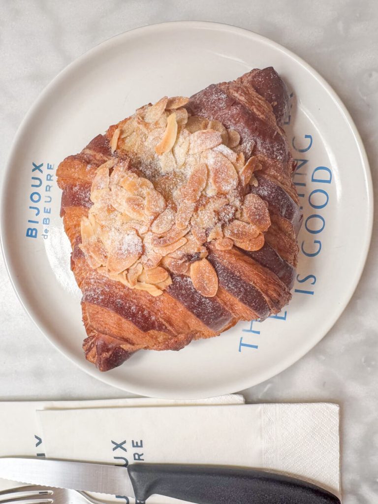 Flaky buttery croissant with almonds served on a plate with a fork and knife