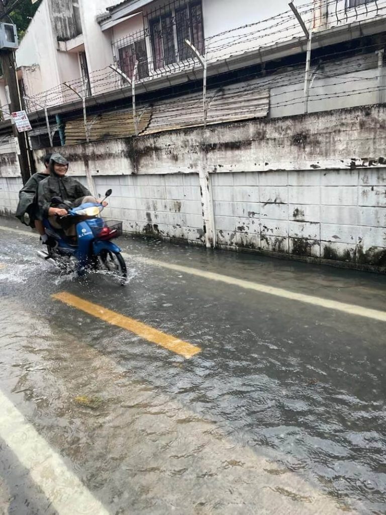 Rainy soi flooded and a motorbike making its way through the high water mark